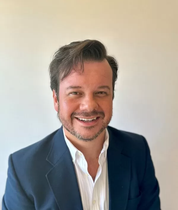 A headshot of Scott Burns smiling, wearing a navy blue blazer and white shirt, set against a plain background.