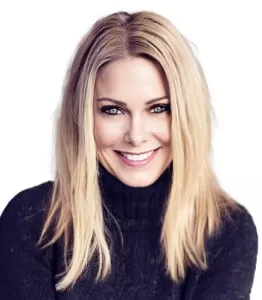 A professional portrait of a smiling The Beckage Firm's Lee Merroet with long blonde hair, wearing a black turtleneck sweater against a white background.