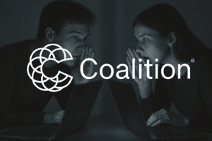 Two professionals whispering into their laptops symbolizing data privacy and cybersecurity risks, with the Coalition logo representing proactive cyber insurance policy protection.