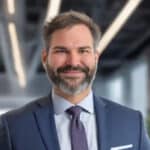 Professional headshot of Kyle Jude, author discussing the hidden costs of cyberattacks on small businesses, the risks of cyberattacks and the protective measure cyber liability insurance represents, shown in a modern office setting.