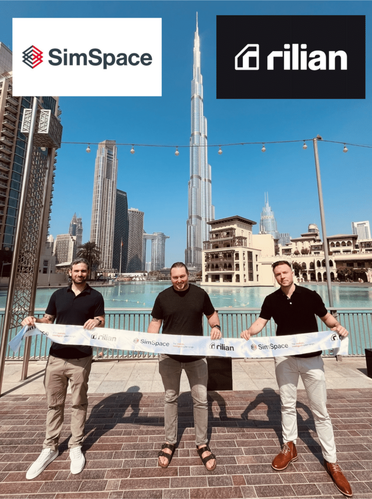 Christian Schnedler, Graham Westbrook, and Jason Rivera hold a SimSpace–Rilian ribbon-cutting in Dubai during a cybersecurity partnership launch.