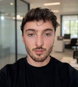 Mitchell Spicer, co-founder and COO of Revelion, wearing a black T-shirt in a bright open-plan office